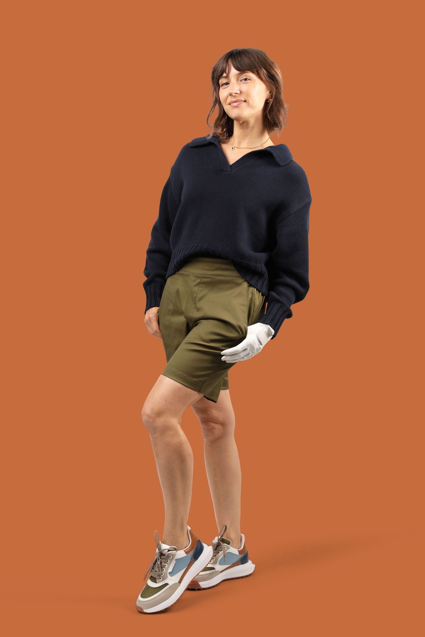 Women's golfer in sustainably made olive green shorts and navy sweater.